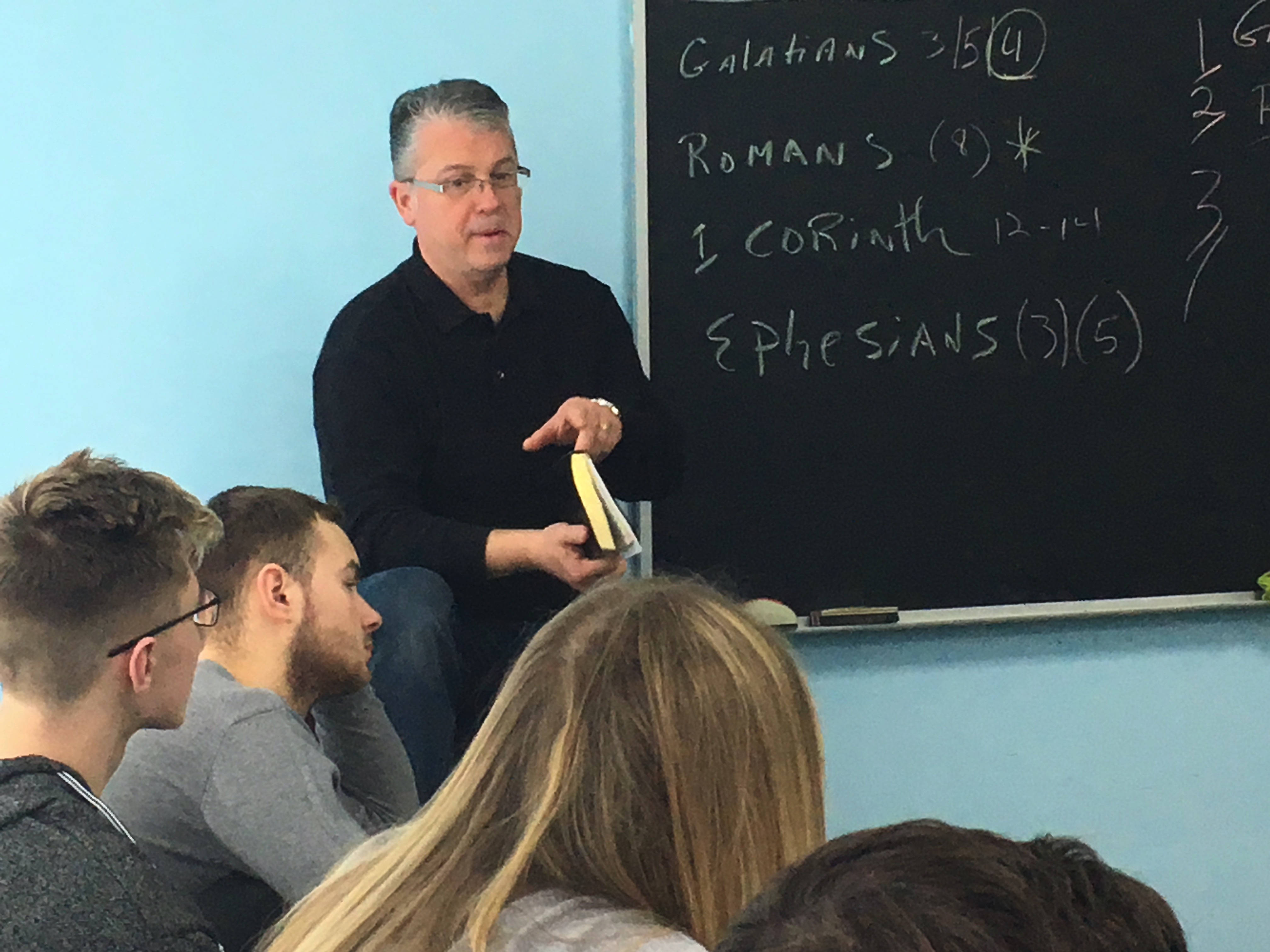 Man speaking to students in front of chalk board