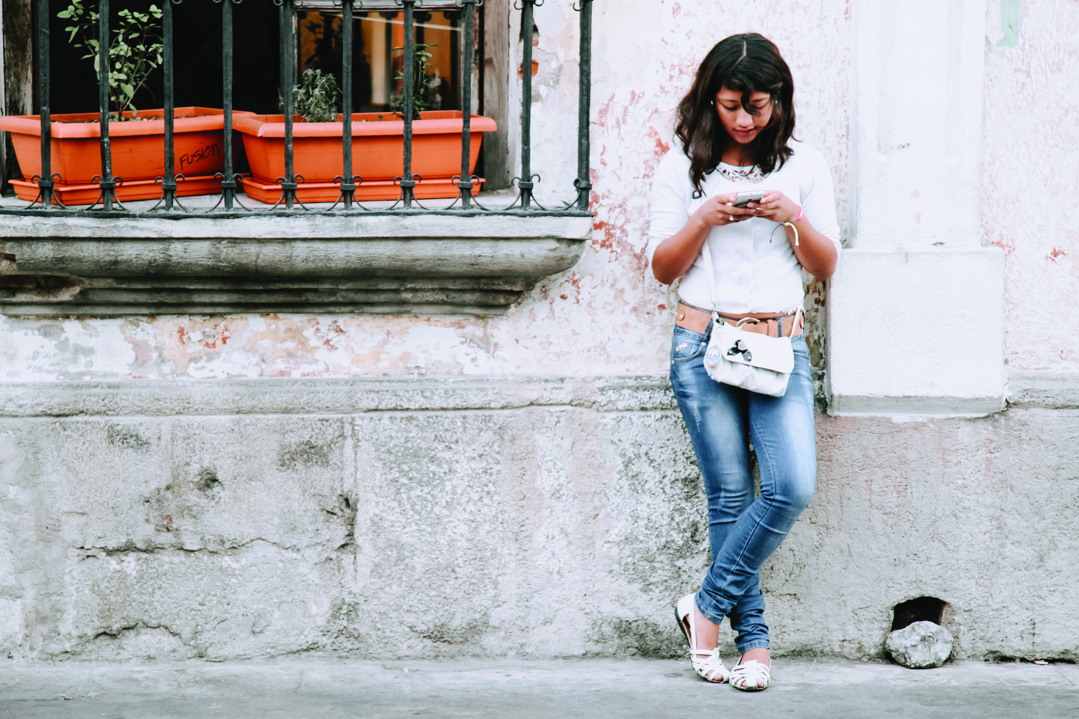 Photo of a girl leaning against the wall and texting on her phone.