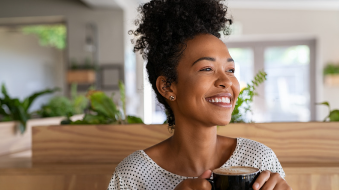 A young woman holding a latte smiles while she looks off into the distance