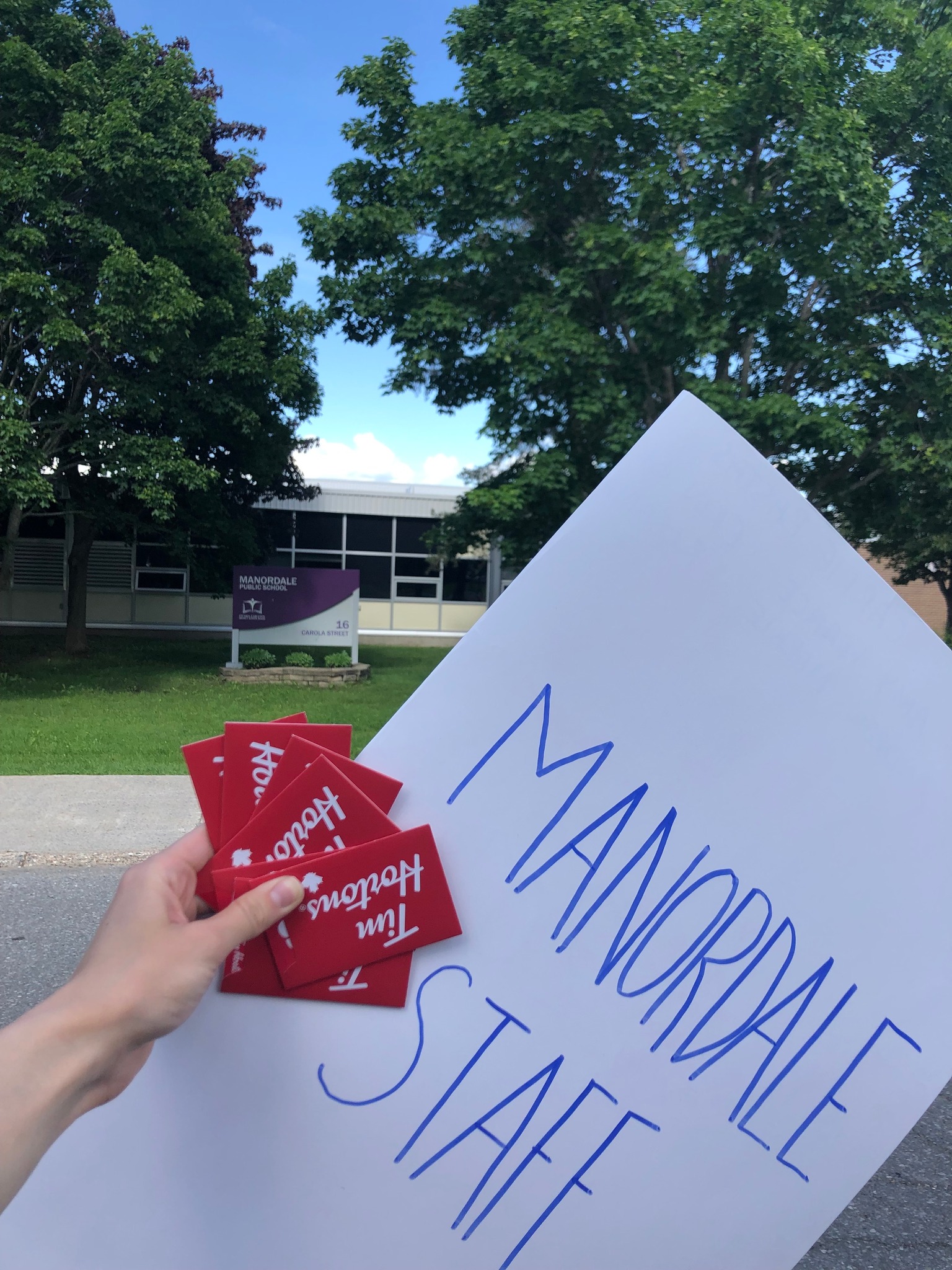 A person holding a sign that reads "Manordale Staff" and Tim Horton's gift cards.